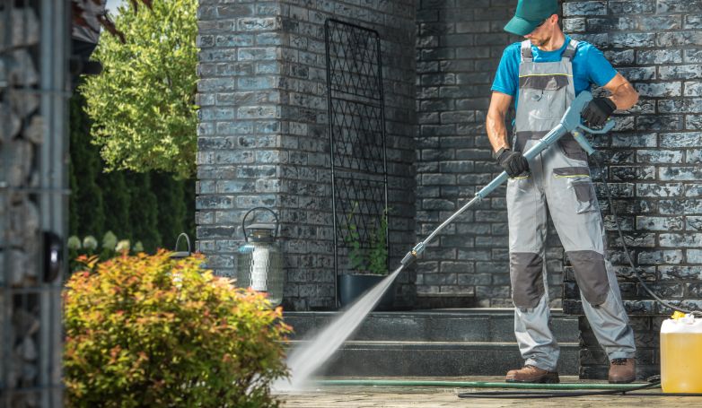 A workman is cleaning the driveway with the pressure washer to preserve its durability.
