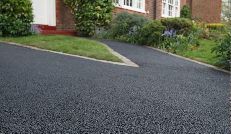 A clean and smooth asphalt driveway with plants and grass