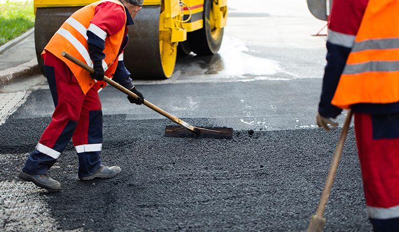 A worker installing asphalt over gravel on a driveway
