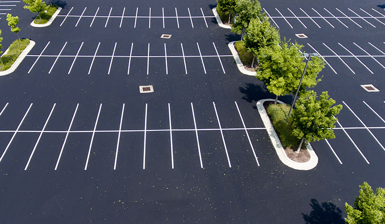 A beautiful asphalt parking lot with green trees at the side.