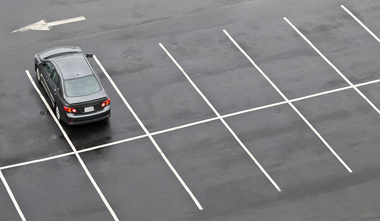 A lonely black car on the wet parking lot asphalt.