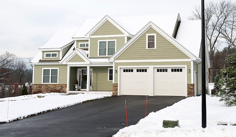 A simple house surrounded by snow with a two car width driveway