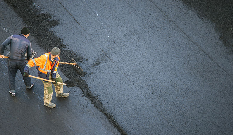A workers flatten the surface of asphalt road.