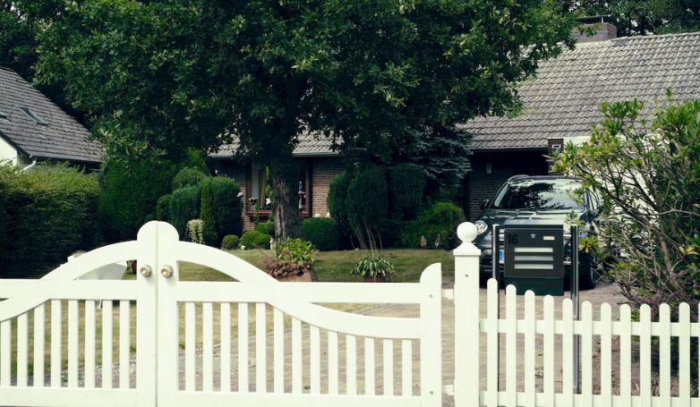 A white wooden gate on a driveway with black luxury car.