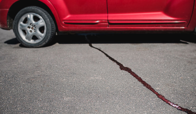 A red car is leaking oil in the parking lot where it is parked. 