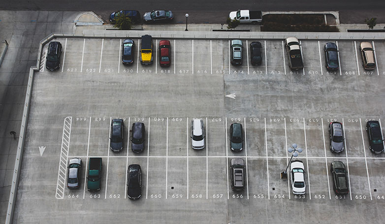 A different cars parked on concrete parking lot with striping guides.