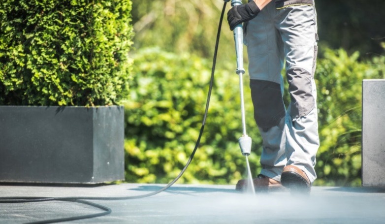A worker cleans the concrete driveway using water pressure.