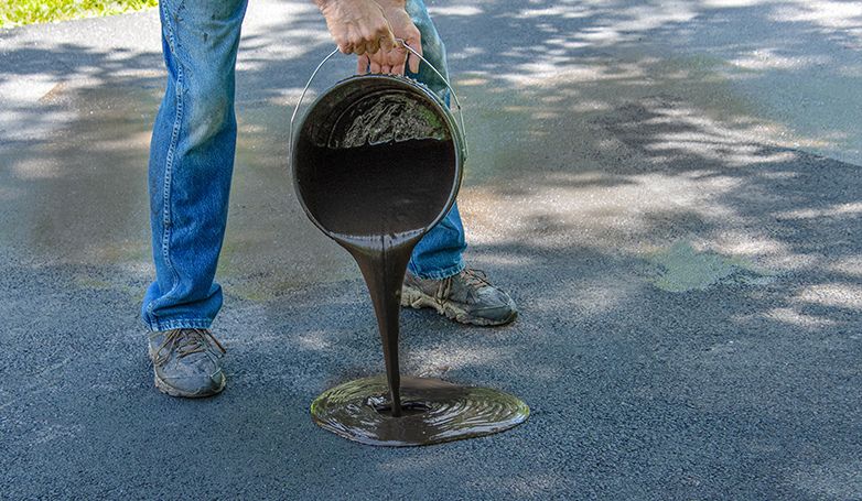 The owner seals the small pothole using a seal coat on his asphalt driveway. 