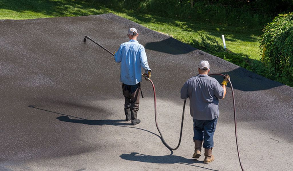 The workers apply seal coating on the newly resurfaced concrete driveway.