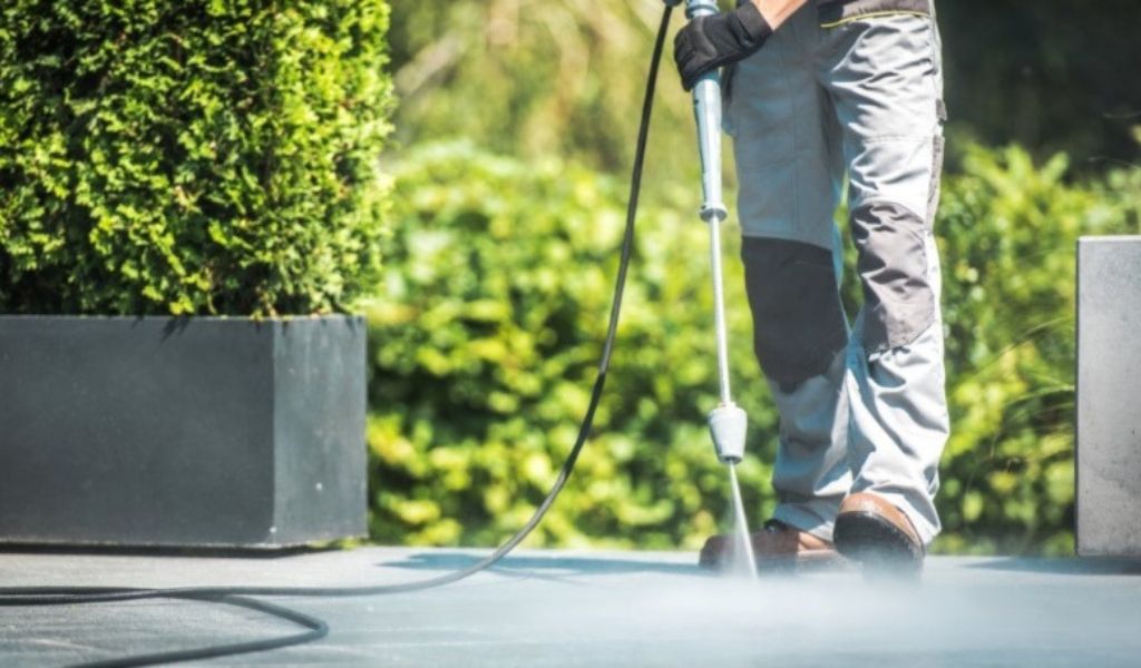 The worker cleans the concrete driveway using a pressure washer.