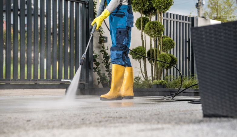 The worker is cleaning the concrete driveway before applying asphalt