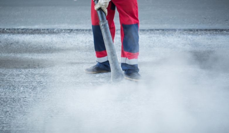 The worker is regularly and constantly cleaning the newly treated asphalt