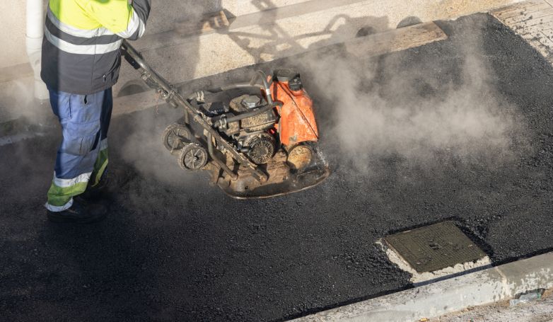 The worker is compacting new asphalt after repairing alligator cracks