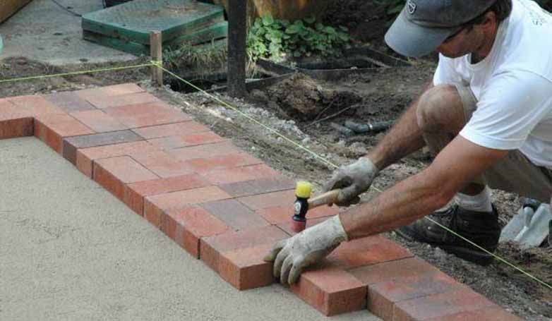 A man installing solid brick for his driveway edging.