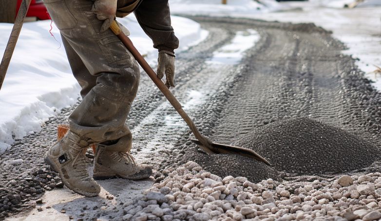 The worker is paving the gravel driveway in winter