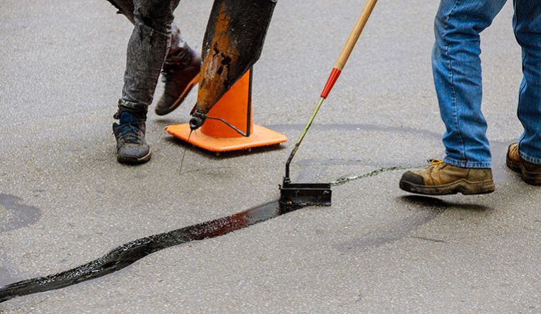 Workers filling cracks on the tar and chip driveway
